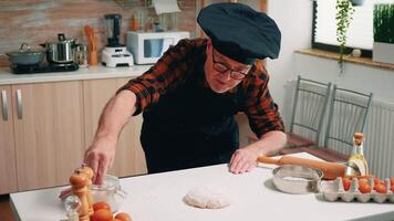 pensionato panettiere uomo setacciare Farina su chopping tavola fabbricazione Impasto a casa. anziano anziano capocuoco con bonete e uniforme aspersione, setacciare, diffusione ingredienti di mano, cottura al forno fatti in casa Pizza e pane video