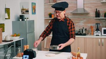 Man cooking in front of professional digital mirrorless camera with microphone recording blog. Retired chef influencer using internet technology communicating, shooting blogging on social media video