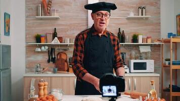 en utilisant métallique tamis tandis que cuisine vivre enregistrement Nouveau culinaire épisode. retraité blogueur chef influenceur en utilisant l'Internet La technologie communicant tournage bloguer sur social médias avec numérique équipement video