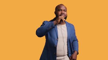 Upbeat african american singer holding microphone, performing tunes, isolated over yellow studio background. Energetic musician singing to imaginary crowd, doing karaoke, camera B video