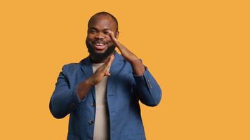 Cheerful african american man asking for timeout, doing hand gestures, halting activities. Friendly upbeat person doing pause sign gesturing, wishing for break, studio background, camera A video