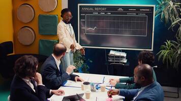 Marketing assistant presenting infographics in a status update meeting, studying data to establish key performance indicators. African american employee operating interactive board. Camera B. video