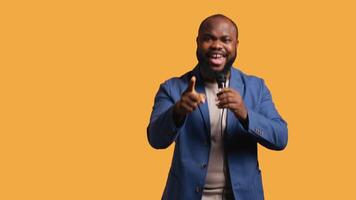 Aggressive lecturer holding motivational speech using microphone, gesturing with hands, isolated over studio background. Speaker urging spectators to take action, doing speech using mic video