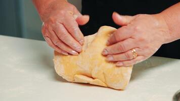 fechar acima do mãos levando uma ampla peça do pastelaria, fazer pães a partir de massa. aposentado idosos padeiro com bonete mistura ingredientes com peneirado trigo farinha amassar para cozimento tradicional bolo e pão. video