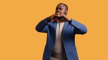 Portrait of jolly friendly african american man doing heart symbol shape gesture with hands. Cheerful nurturing BIPOC person showing love gesturing, isolated over studio background, camera B video