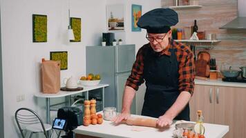 Retired chef recording a new culinary episode using the dough rolling pin. Retired blogger influencer using internet technology communicating shooting blogging on social media with digital equipment video