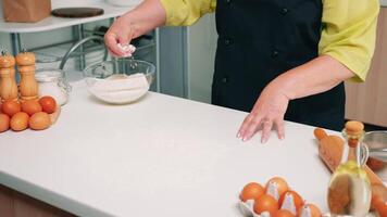 fabbricazione Impasto di donna mani a casa nel cucina utilizzando Grano Farina. pensionato anziano panettiere con bonete e uniforme aspersione, setacciare, diffusione rew ingredienti cottura al forno fatti in casa Pizza e pane. video