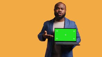 Portrait of african american man doing influencer marketing using green screen lapyop, studio background. BIPOC person holding empty copy space mockup notebook, doing advertising camera B video