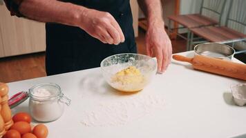 Process of preparing the pastry dough made by man baker. Retired elderly chef with uniform sprinkling, sieving sifting raw ingredients by hand and mixing with flour for baking homemade pizza, bread. video