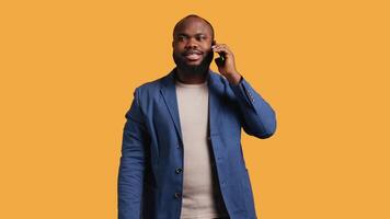 Joyous man with positive emotion, enjoying talking with friends phone call using smartphone, studio background. Happy african american person with smile on face during telephone call, camera B video