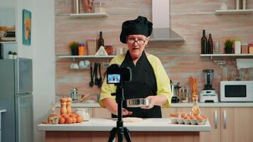 glücklich Alten Bäcker Frau filmen Kochen vlog im Zuhause Küche. im Ruhestand Blogger Koch Influencer mit Internet Technologie kommunizieren, Schießen Bloggen auf Sozial Medien mit Digital Ausrüstung video
