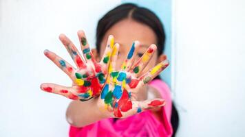 Cute little girl with colorful painted hands on wall background photo