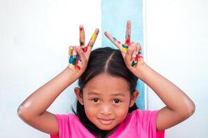 linda pequeño niña con vistoso pintado manos en pared antecedentes foto