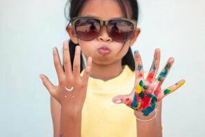 Cute little girl with colorful painted hands on wall background photo