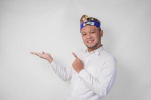 Attractive Balinese man in white shirt and traditional headdress called udeng pointing to the copy space on the left and right side while smiling cheerfully photo