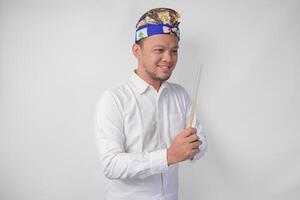 Balinese man wearing traditional headdress called udeng doing paying respect gesture while holding praying incense on isolated white background photo