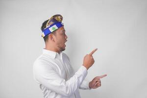 Attractive Balinese man in white shirt and traditional headdress called udeng pointing to the copy space on the left and right side while smiling cheerfully photo