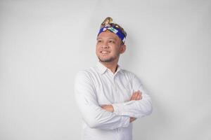 retrato de un balinés vistiendo tradicional tocado llamado udeng posando con un cruzado brazos y confidente sonrisa terminado aislado blanco antecedentes foto