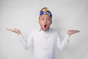 Surprised Balinese man in white shirt and traditional headdress called udeng pointing to the copy space on the left and right side photo