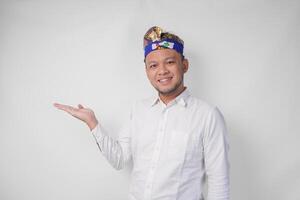 Attractive Balinese man in white shirt and traditional headdress called udeng pointing to the copy space on the left and right side while smiling cheerfully photo