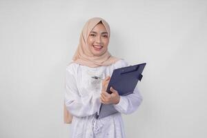 Smiling young Asian Muslim woman wearing white dress and hijab holding a document, Isolated by white background. Ramadan and Eid Mubarak concept photo