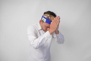 Balinese man wearing traditional headdress called udeng doing praying hand or paying respect gesture on isolated white background photo