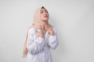 Tired Asian Muslim woman in white dress and hijab holding her neck feeling thirsty waiting for iftar to drink. Ramadan concept photo