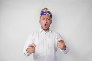 Portrait of handsome young Balinese man wearing traditional headdress called udeng with shocking expression, isolated over white background photo