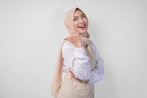 Excited young Asian Muslim woman in hijab and cream apron pointing to the empty copy space on the left and right side. Ramadan advertisement concept photo