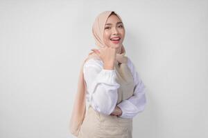 Excited young Asian Muslim woman in hijab and cream apron pointing to the empty copy space on the left and right side. Ramadan advertisement concept photo