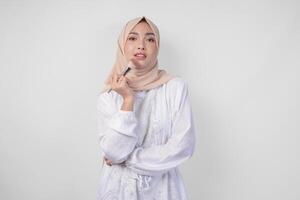 Beautiful young Asian Muslim woman wearing white dress and hijab applying make up using brush. Fashion and cosmetics beauty concept photo