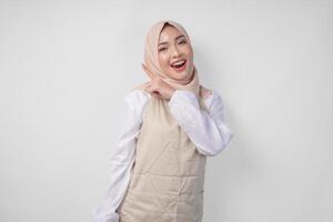 Excited young Asian Muslim woman in hijab and cream apron pointing to the empty copy space on the left and right side. Ramadan advertisement concept photo