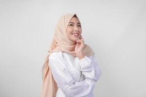 Portrait of beautiful Asian Muslim woman with natural make-up wearing white dress and hijab posing on white background in studio. Facial skin care, female beauty concept photo