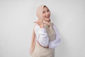 Excited young Asian Muslim woman in hijab and cream apron pointing to the empty copy space on the left and right side. Ramadan advertisement concept photo