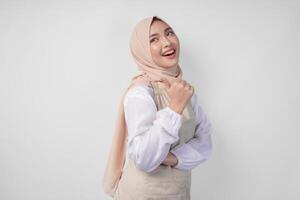 Excited young Asian Muslim woman in hijab and cream apron pointing to the empty copy space on the left and right side. Ramadan advertisement concept photo