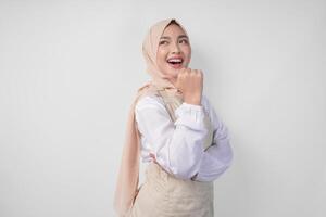 Excited young Asian Muslim woman in hijab and cream apron pointing to the empty copy space on the left and right side. Ramadan advertisement concept photo