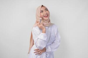 Beautiful young Asian Muslim woman wearing white dress and hijab applying make up using brush. Fashion and cosmetics beauty concept photo