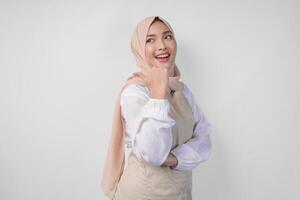 Excited young Asian Muslim woman in hijab and cream apron pointing to the empty copy space on the left and right side. Ramadan advertisement concept photo