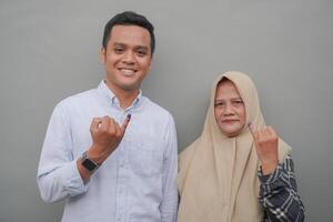 Portrait of excited Indonesian family showing the little finger dipped in purple ink after voting for general election or Pemilu for president and government, isolated grey background photo