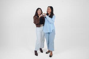 Two young Asian women expressing their tender feelings, shapes heart gesture expresses her love, isolated by white background. Friendship concept. photo