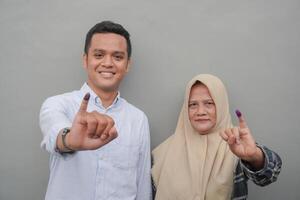 retrato de emocionado indonesio familia demostración el pequeño dedo sumergido en púrpura tinta después votación para general elección o pemilu para presidente y gobierno, aislado gris antecedentes foto