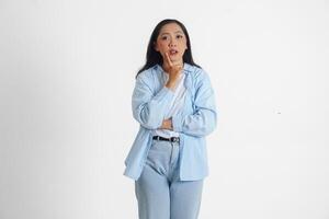 A thoughtful Asian woman wearing blue shirt is imagining her thoughts, isolated by white background. photo