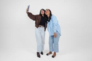 Female friends laughing and taking a fun selfie isolated by white background photo