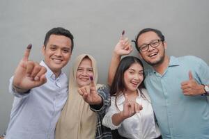 retrato de emocionado indonesio familia demostración el pequeño dedo sumergido en púrpura tinta después votación para general elección o pemilu para presidente y gobierno, aislado gris antecedentes foto