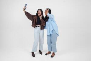 Female friends laughing and taking a fun selfie isolated by white background photo