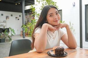 joven asiático mujer participación y demostración un negro plato de rosquilla Pastelería llamado cromboloni con chocolate relleno para bocadillo tiempo, sonriente con un contento y alegre expresión foto