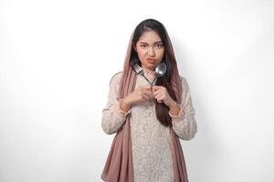 Beautiful Asian woman in veil hijab holding eating cutlery and making a refusal or rejection sign, saying no, asking to stop, standing over isolated white background photo