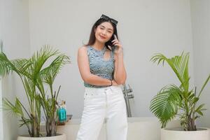 Happy Asian woman standing by the pool while calling and talking on a mobile phone with a cheerful smile on the face photo