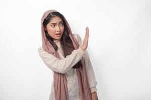 Young Asian Muslim woman wearing veil hijab gesturing a no rejection, refuse using hands and fingers, isolated by white background. Ramadan and Eid Mubarak concept photo