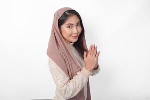 Smiling young Asian Muslim woman gesturing Eid Mubarak greeting from side view isolated over white background photo